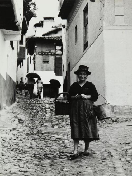 Mujer con cubo y cesto en la calle de un pueblo