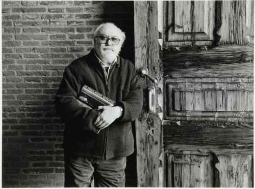 Rafael Sanz Lobato posa con libro de retratos de Lee Friedlander, junto a portón de madera