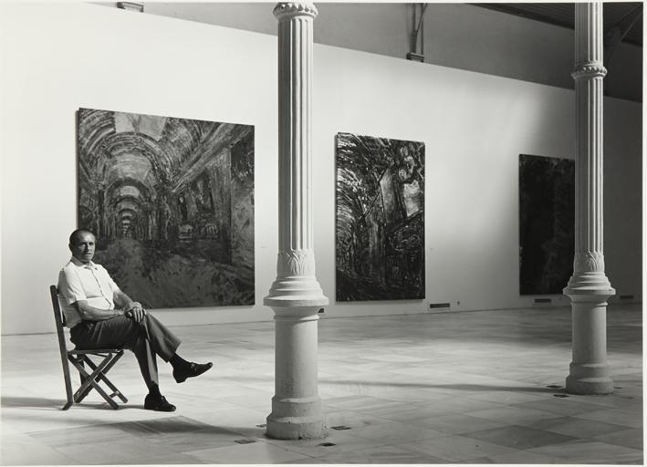 Retrato de hombre mayor sentado en una silla en una sala de exposiciones