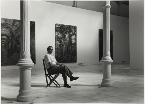 Retrato de hombre mayor sentado en una silla en una sala expositiva