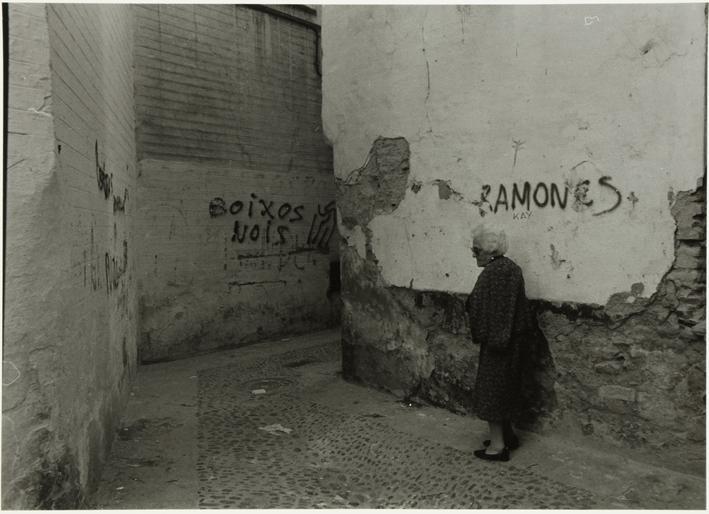 Mujer mayor en una calle, paredes con pintadas